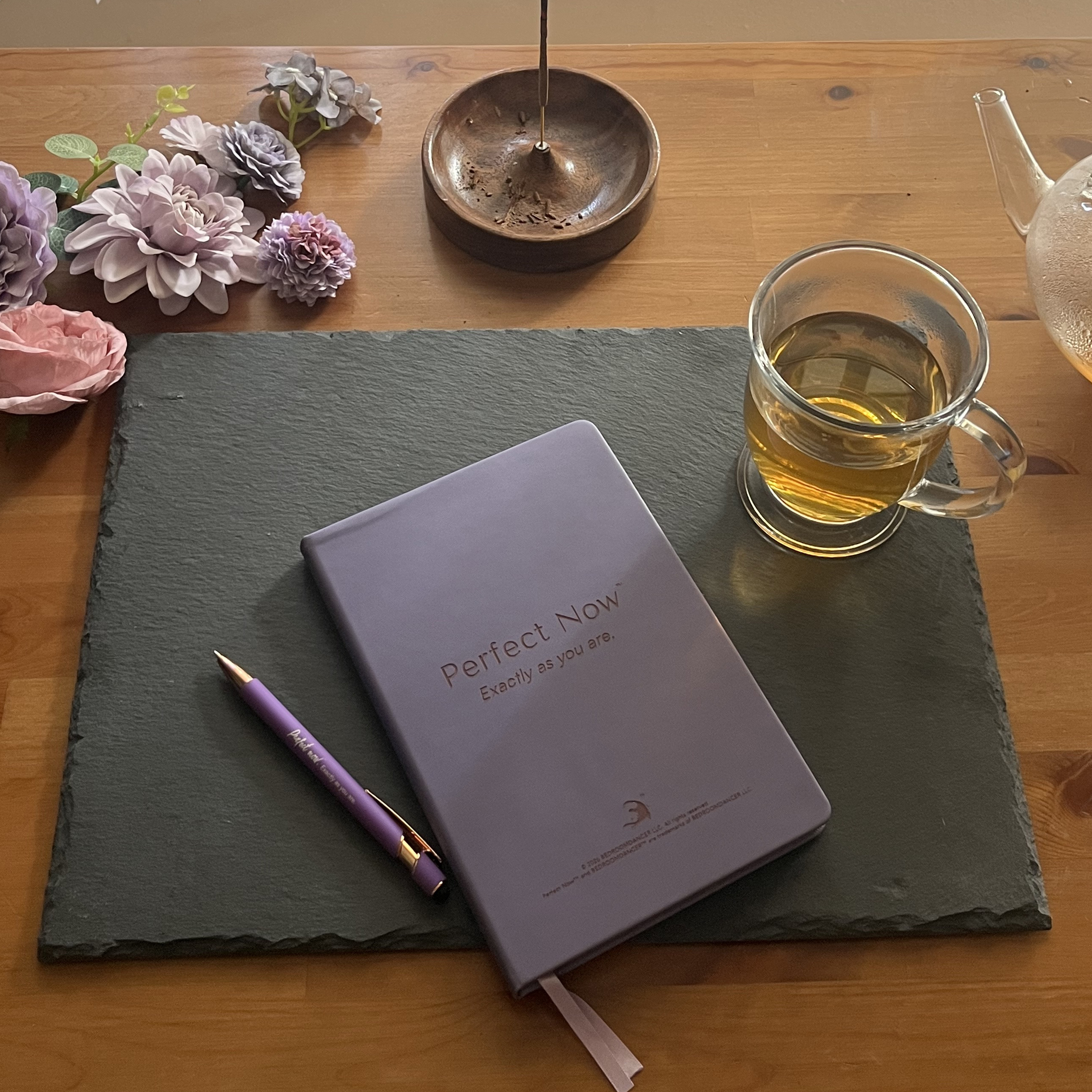 Violet leather journal and engraved pen resting on slate with lavender